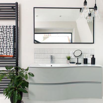 A modern bathroom vanity with black framed mirror and black metal heated towel rail with geometric-patterned towel decor and houseplant