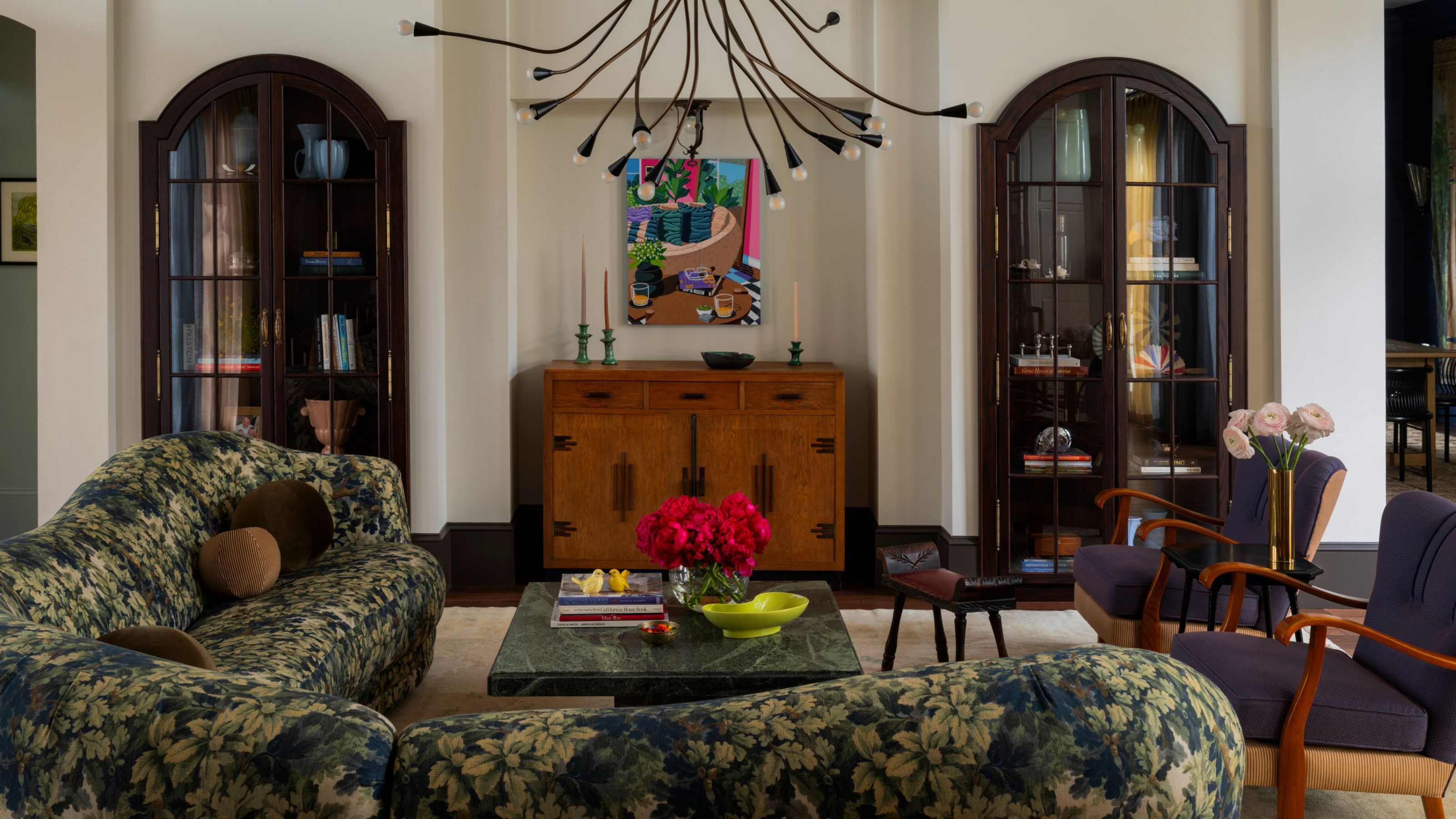 a white painted living rom with large dark wooden arched alcove cabinetry, a vintage credenza, large sputnik chandelier, and a curved tapestry print sofa