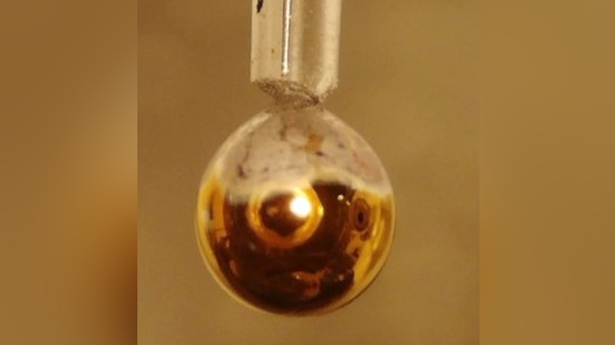 Ein Tropfen flüssigen Metalls wird von einer dünnen Wasserschicht bedeckt, die sich nach der Aufnahme metallischer Qualitäten goldgelb verfärbt hat