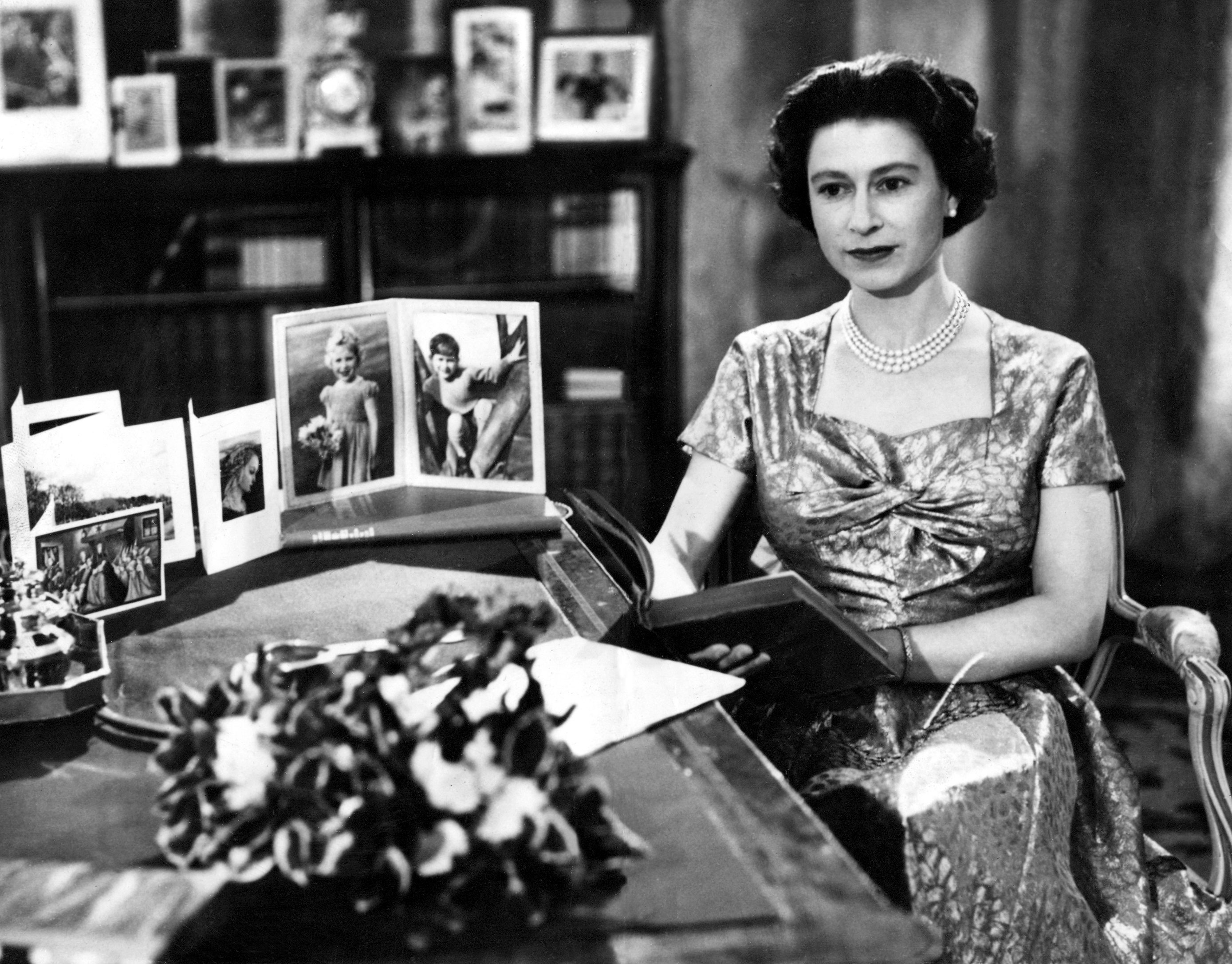 Elizabeth II posing at her desk surrounded by family photographs