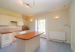 Before picture of kitchen with grey floor, magnolia walls, cream kitchen units and wooden island