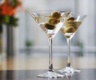 A martini glass with olives in and some flowers in the background