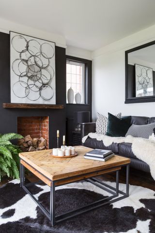 A black and white living room with bubble-effect wall art , cow print rug, disused fireplace and large black-framed mirror