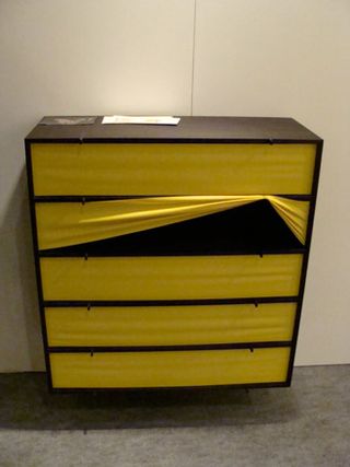 Brown shelving unit with yellow rubber covers photographed against a cream wall and grey vinyl floor