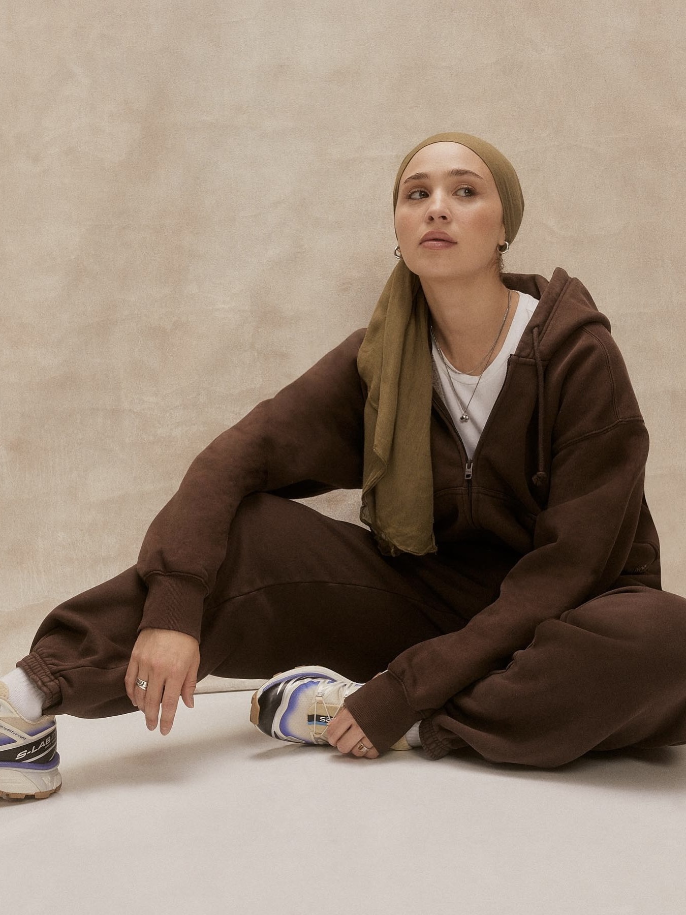 maria alia wearing a brown lounge set with a white tee, salomon sneakers, and an olive headscarf