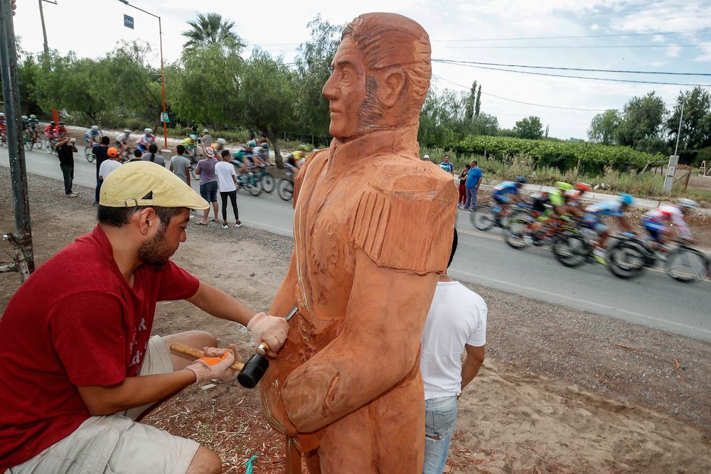 A wooden spectator takes in the scene as the San Juan peloton passes by