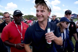 Bacham celebrates with a bottle of beer as he walks off the 18th green