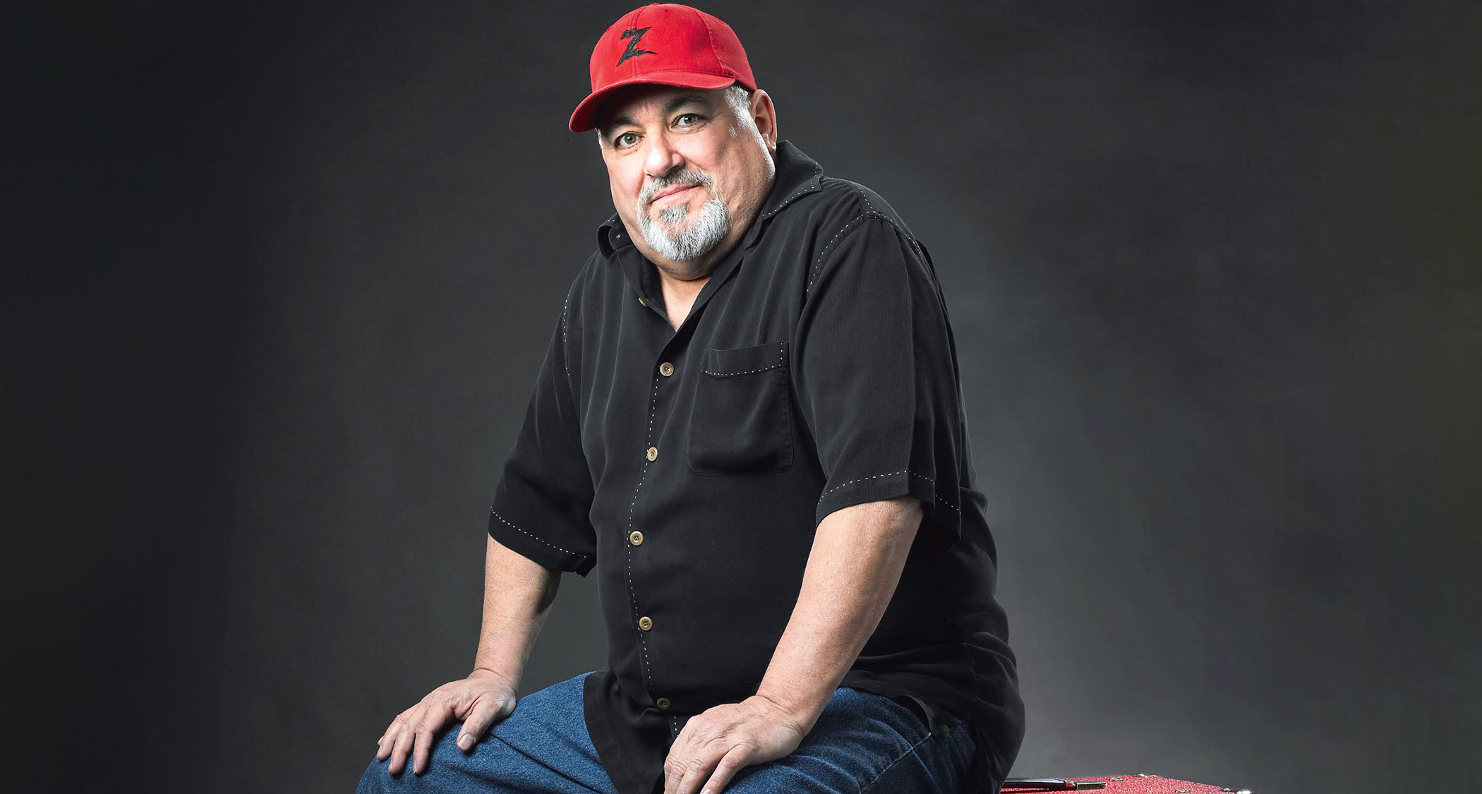 Tube amp guru Mike Zaite of Dr Z Amplification sits on a red cabinet wearing a red Dr Z ballcap.