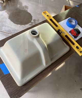 Image of sink basin on wooden dresser vanity with yellow spirit level equipment and blue adhesive tape