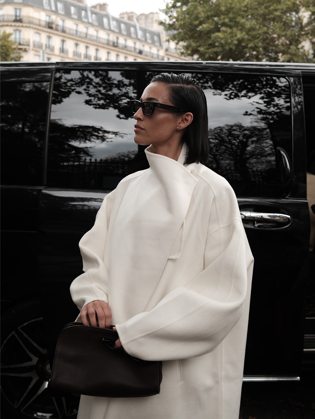 Ariana wears a white coat and a black leather clutch.