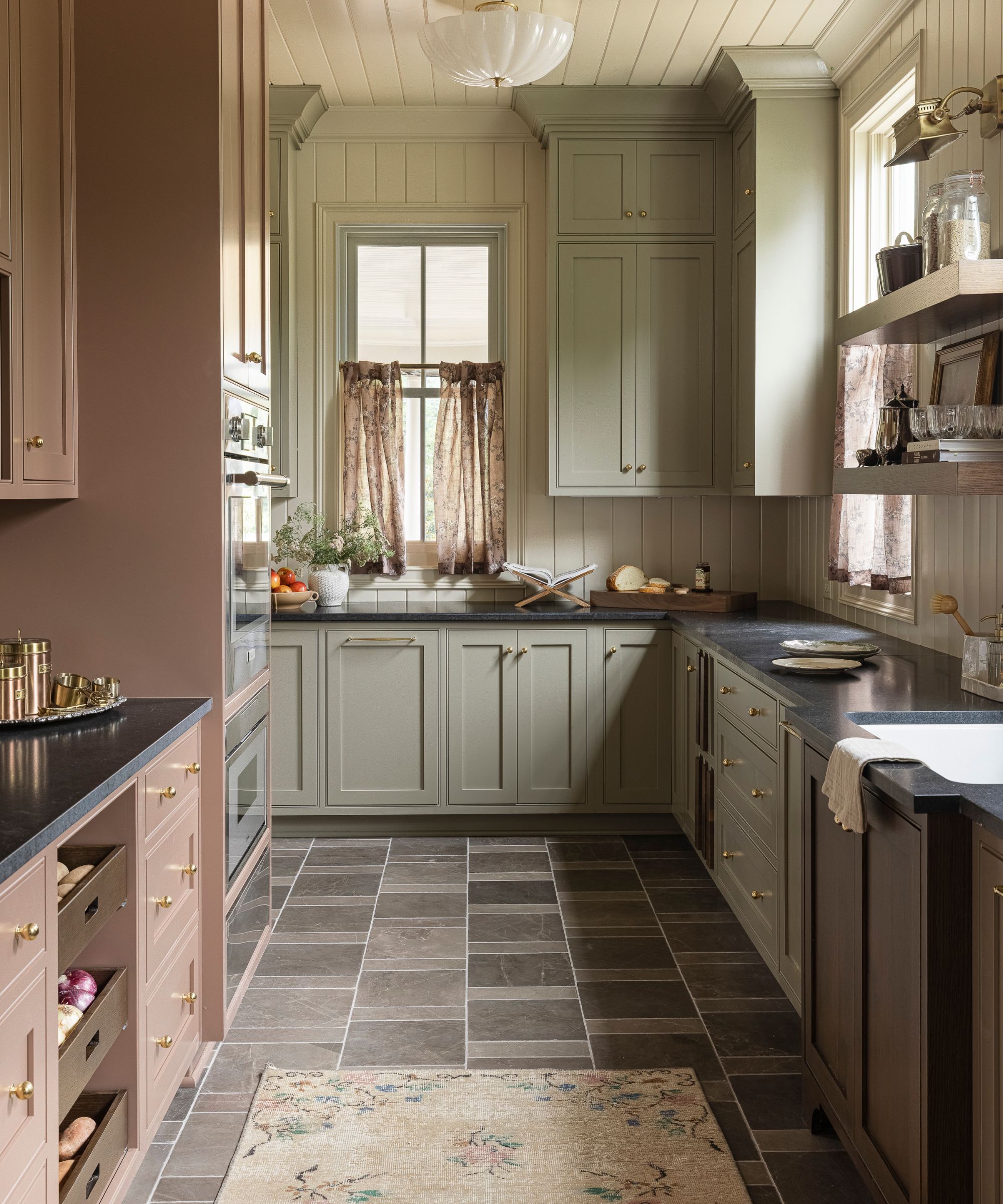Country kitchen with sage green painted cabinetry, a slate tiled floor, pale pink bar area, shiplap walls and ceiling, a floral rug, and a glass pendant light.