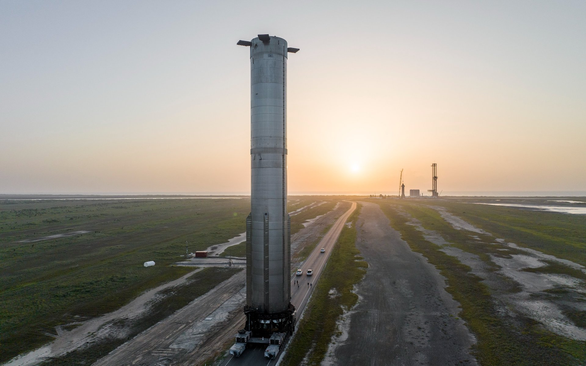 Een extreem zware booster torent hoog boven het vlakke landschap van Texas uit terwijl hij naar het lanceerplatform wordt getransporteerd.