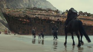 Still from the movie ' Kingdom of the Planet of the Apes' (2024). A presession of armored apes on horseback riding along a beach towards a settlement on a hill.