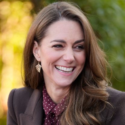 Kate Middleton smiling and wearing a brown coat with leaf earrings