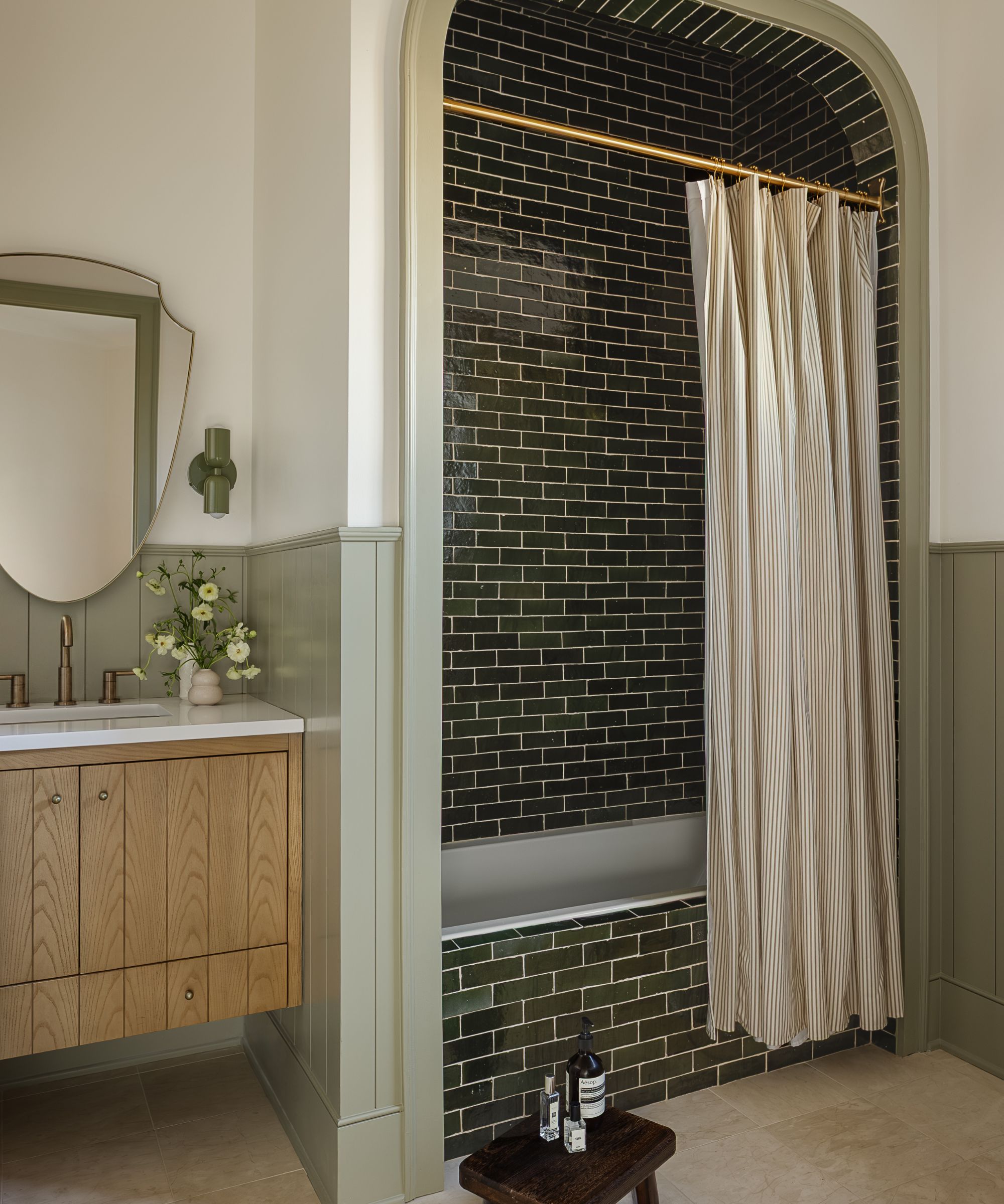 a neutral and soft green guest bathroom with an arched bath nook tiled with green subway tiles