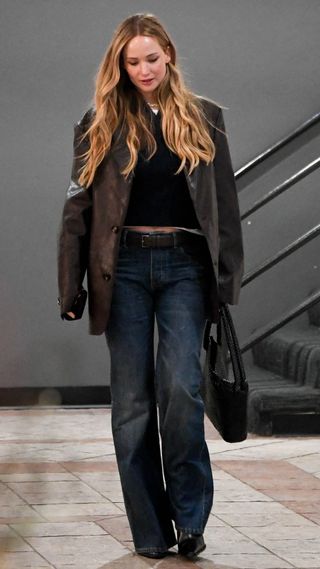 Jennifer Lawrence wearing a brown leather blazer with loose-fitting blue jeans, a black top, and a black handbag