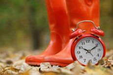 red alarm clock with red rubber boots in the background on an autumn day