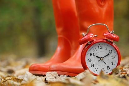 red alarm clock with red rubber boots in the background on an autumn day