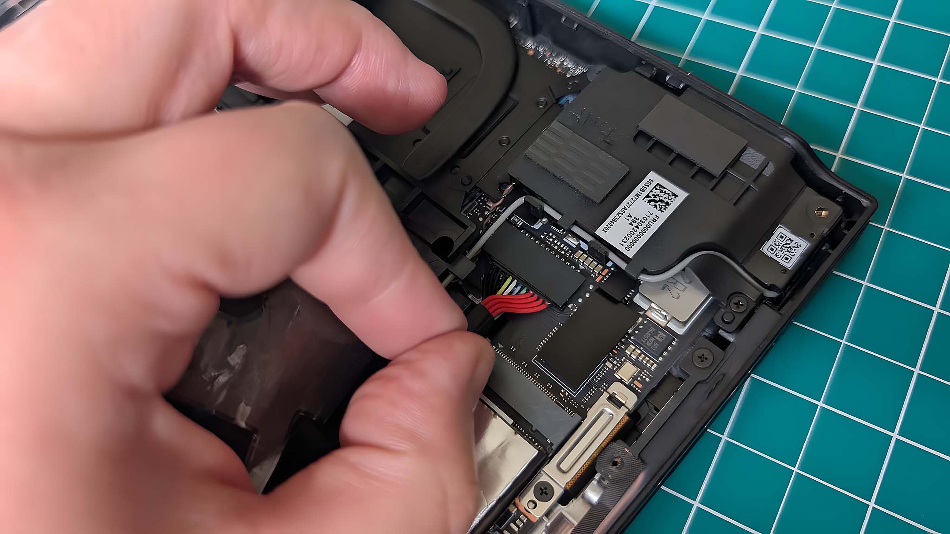 A finger and thumb pulling on the Lenovo Legion Go's battery cables.