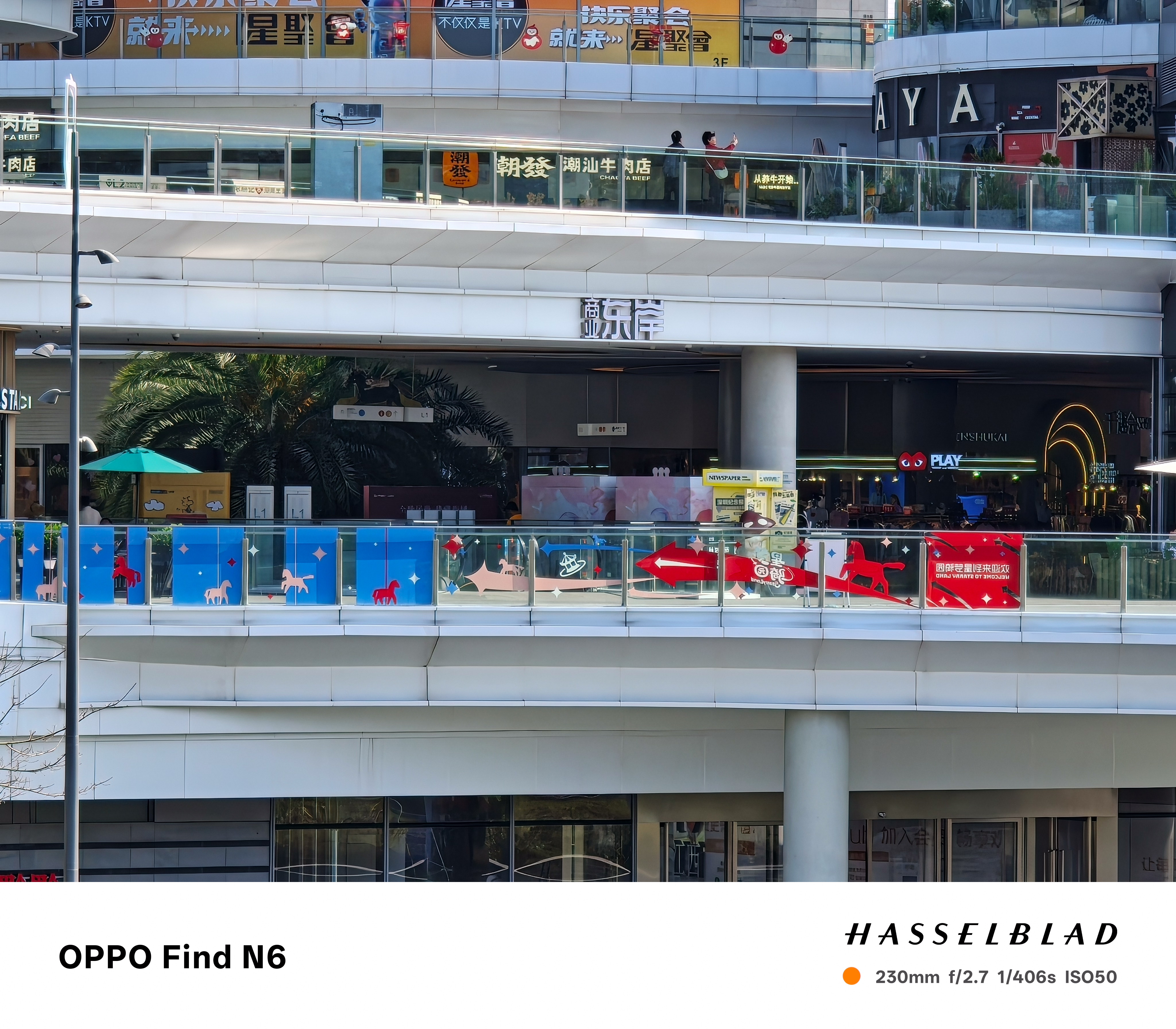 A high-zoom photograph of a commercial building's facade, clearly showing a red "PLAY" sign and colorful decorative graphics on a glass railing. The image captures sharp details of the interior of a shop through the exterior glass.