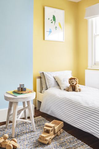 blue and yellow boy's bedroom with wooden toys, stripe rug, white stool, artwork