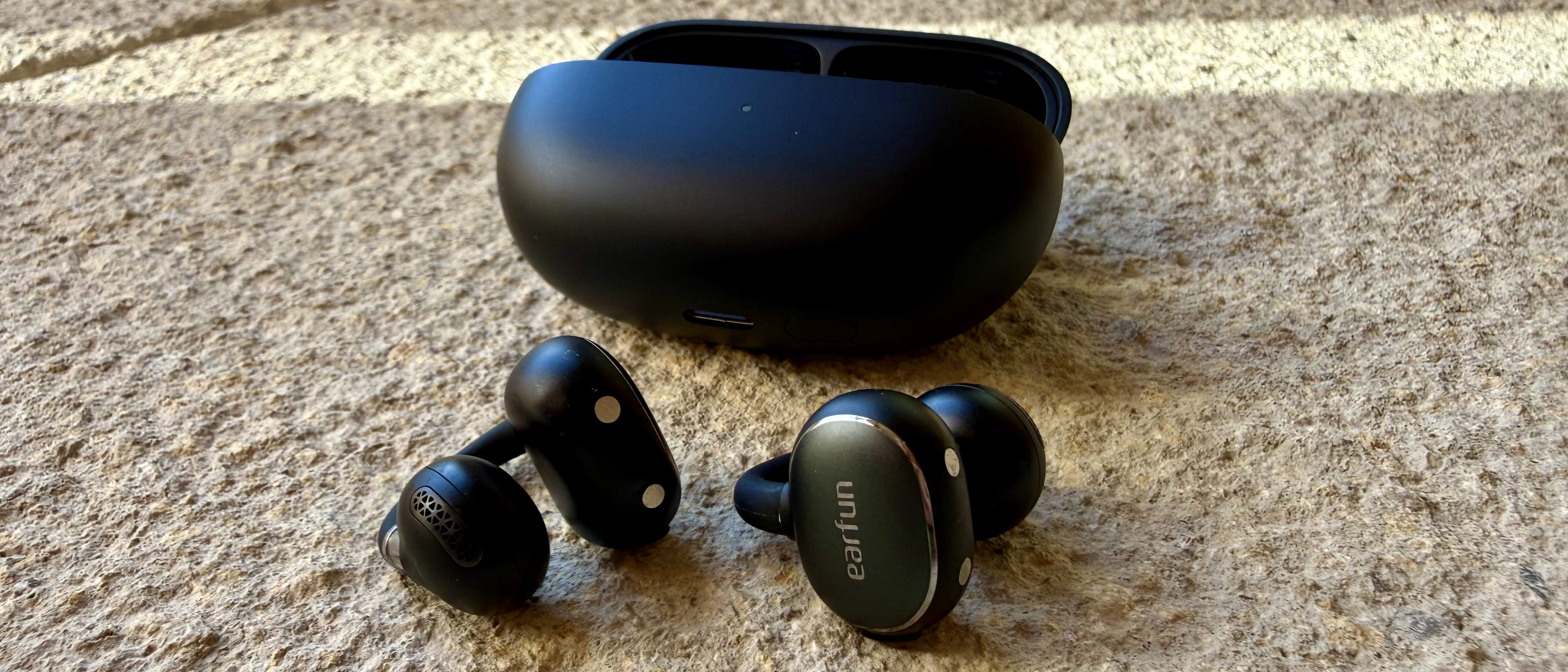 The Earfun Clip 2 earbuds on a stone surface next to its charging case