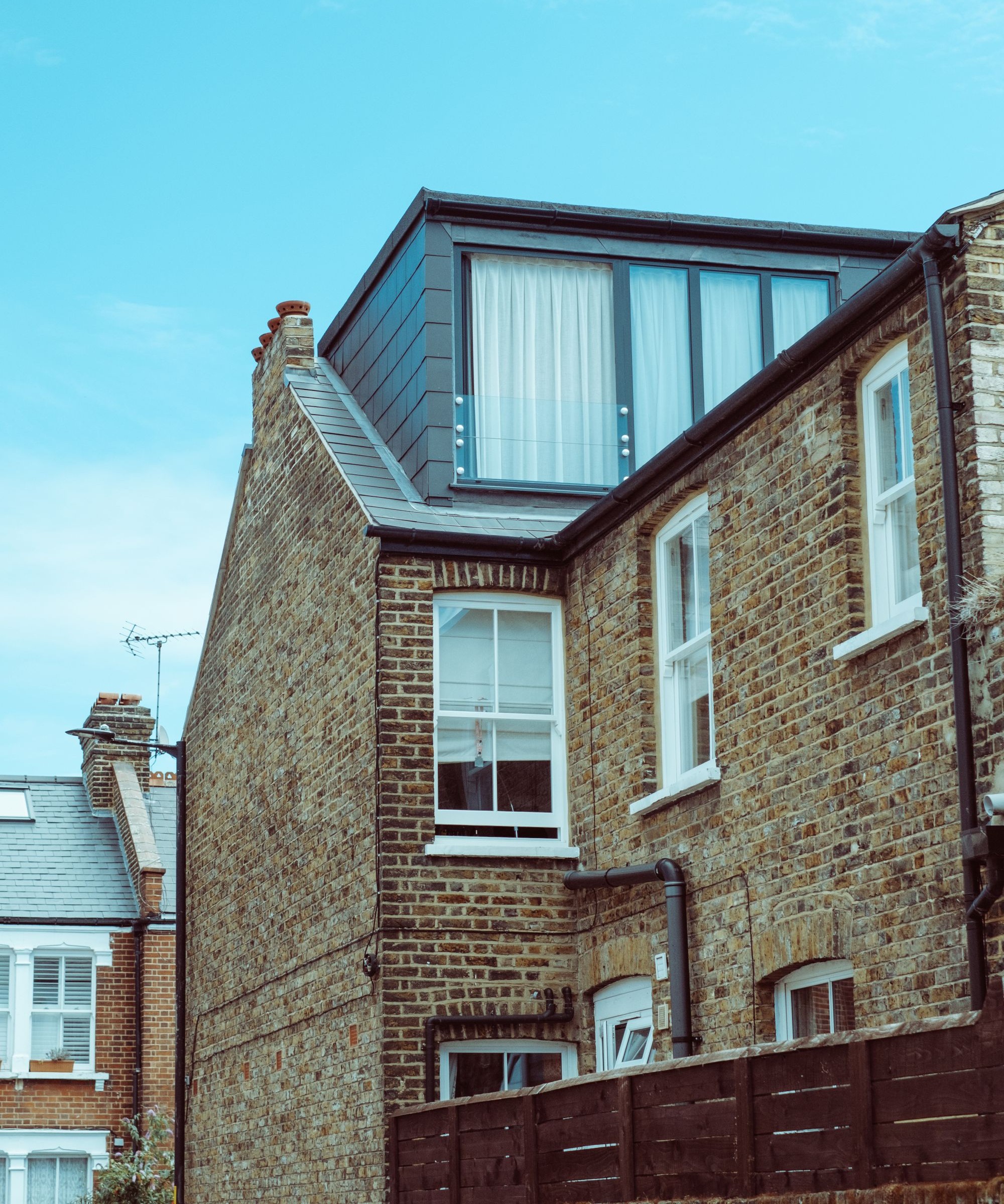A mansard loft conversion as seen from the outside on a brick home with a blue sky above