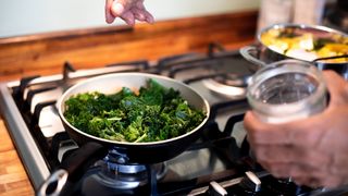 woman cooking greens in a pan