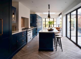 A large, long blue kitchen extension with a kitchen island and stools for seating in front of glass bifold doors