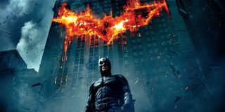 The Dark Knight Batman stands under a burning bat symbol