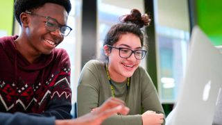 Two students sit in front of a MacBook laptop.