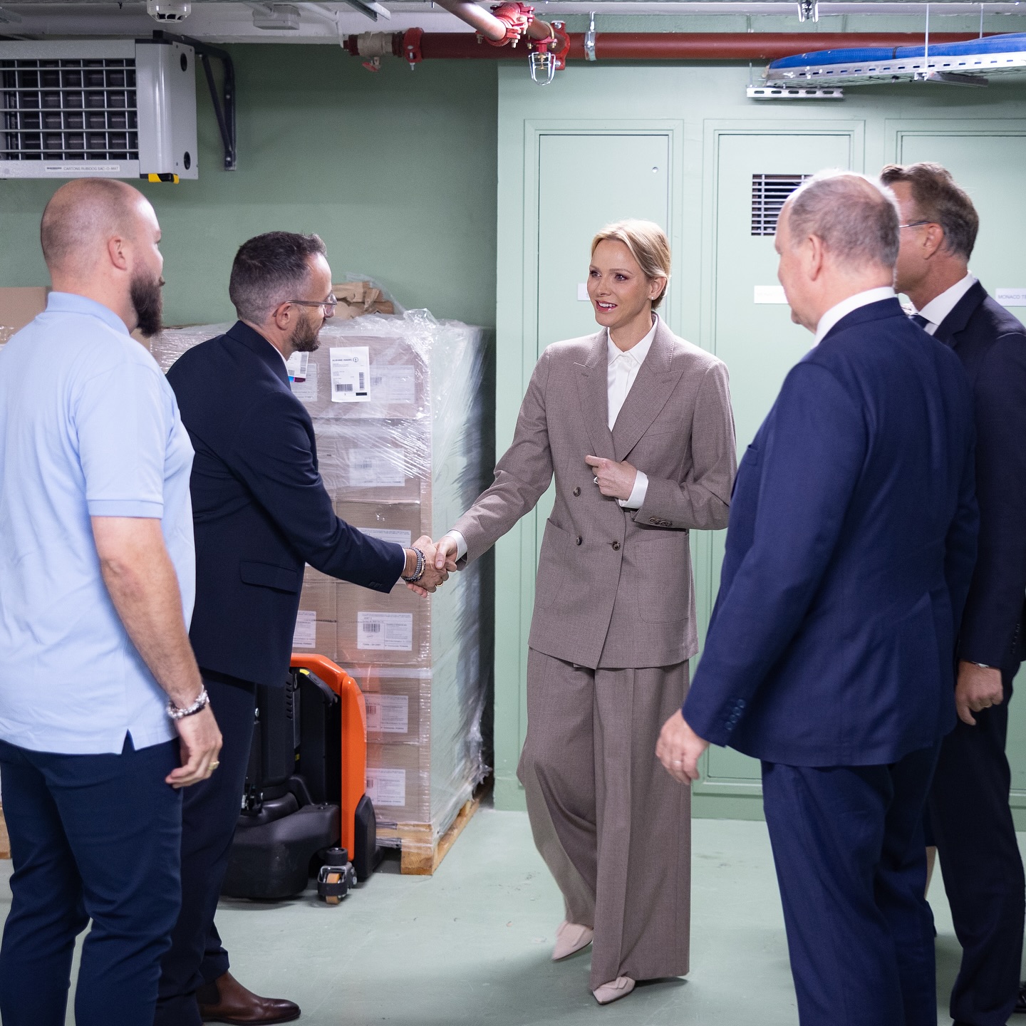 Princess Charlene wearing a baggy suit shaking hands with a man
