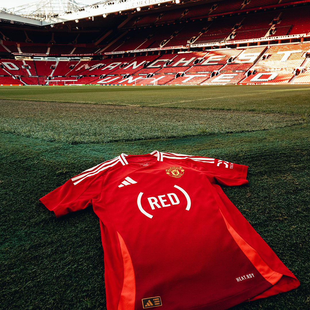 A Manchester United shirt bearing the (RED) Logo on the pitch at Old Trafford