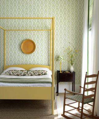 An example of green bedroom ideas showing a bedroom with green and white patterned wallpaper and a yellow four poster bed