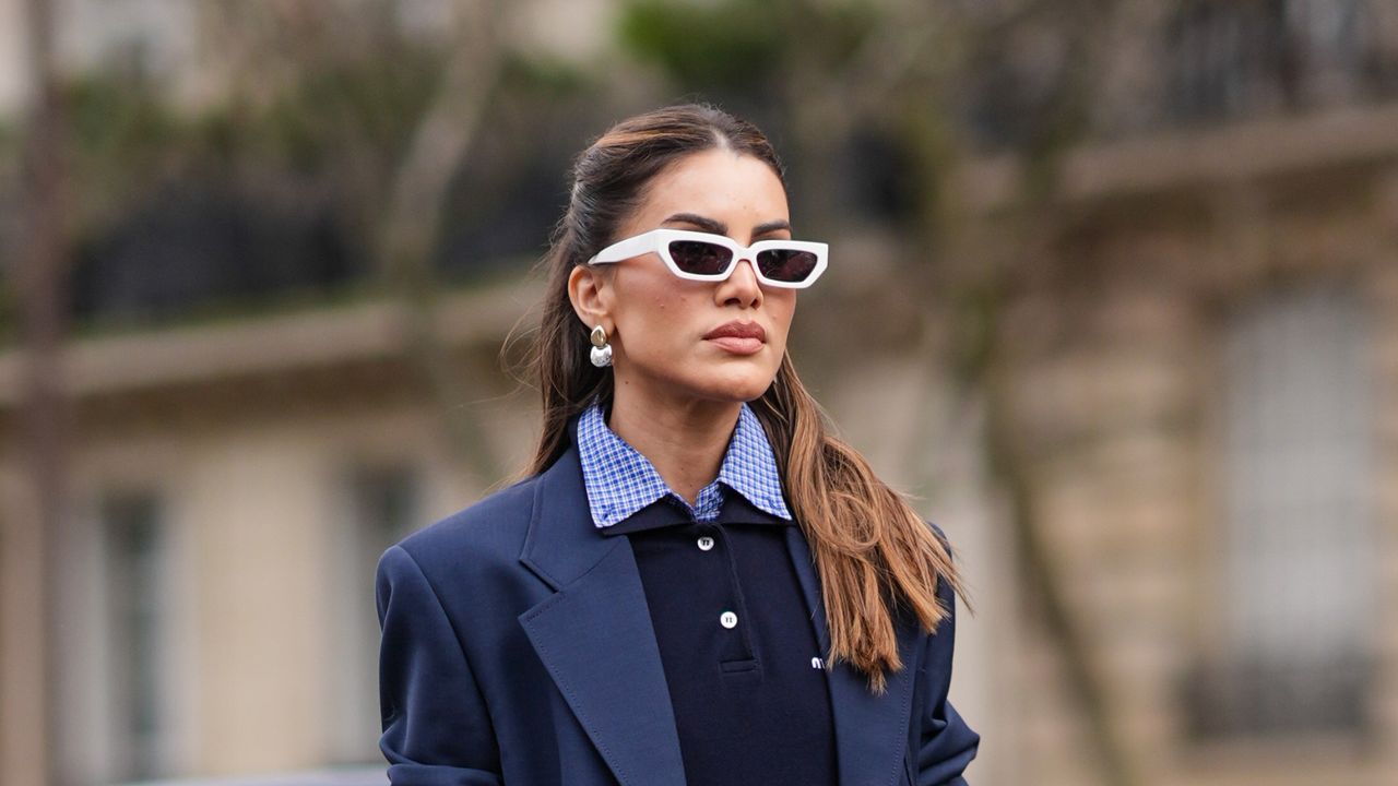 Camila Coelho wears white sunglasses, earrings, a navy blue oversized blazer jacket, a polo shirt, a checkered / checked pattern printed shirt, a white mini skirt , a leather bag, white socks, pointed shoes, outside Miu Miu , during the Womenswear Fall/Winter 2024/2025 as part of Paris Fashion Week on March 05, 2024 in Paris, France