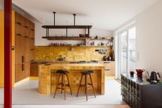 A mustard yellow mainly tiled kitchen with wood floor to ceiling cabinetry on the left
