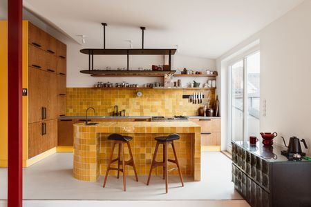 A mustard yellow mainly tiled kitchen with wood floor to ceiling cabinetry on the left