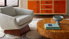 Burl wood coffee table pictured alongside sleek pedestal accent chair and orange glossy credenza