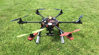 Hexacopter drone built by Adam Juniper sitting on grass, mostly black with red and green front propellors and NAZA flight controller strapped to top