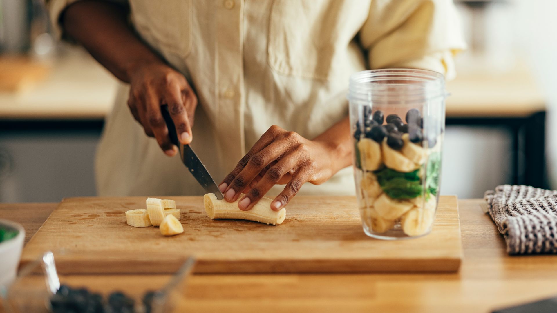 Woman cutting banana into smoothie container with blueberries, the best fruit for gut health