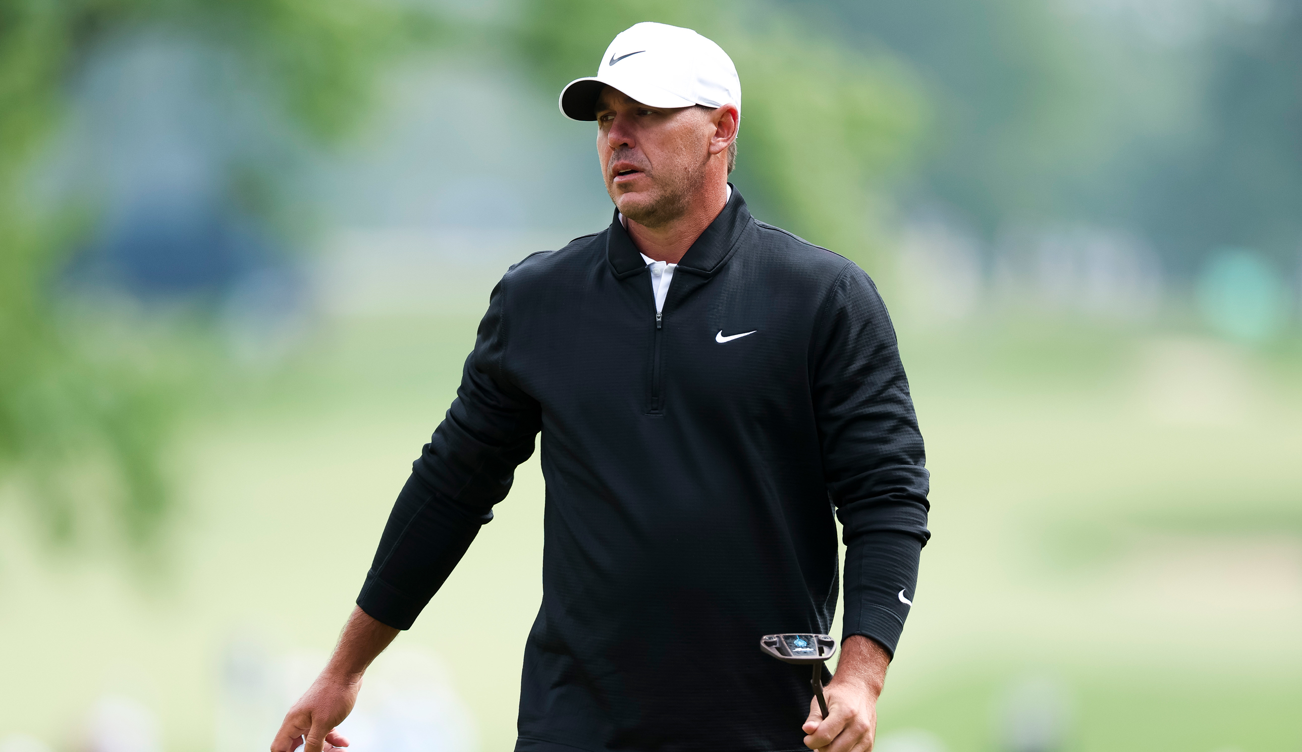 Brooks Koepka walks off the green holding a putter
