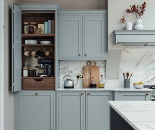 blue kitchen cabinets with floor to cupboard open showing breakfast area with coffee machine, mugs, storage drawer and shelves above with dry goods