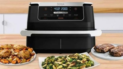 Ninja Foodi FlexBasket Air Fryer on a kitchen counter, surrounded by plates of air fried food.
