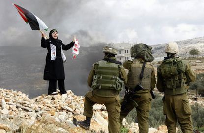 A Palestinian stands in front of Israeli soldiers during a protest.