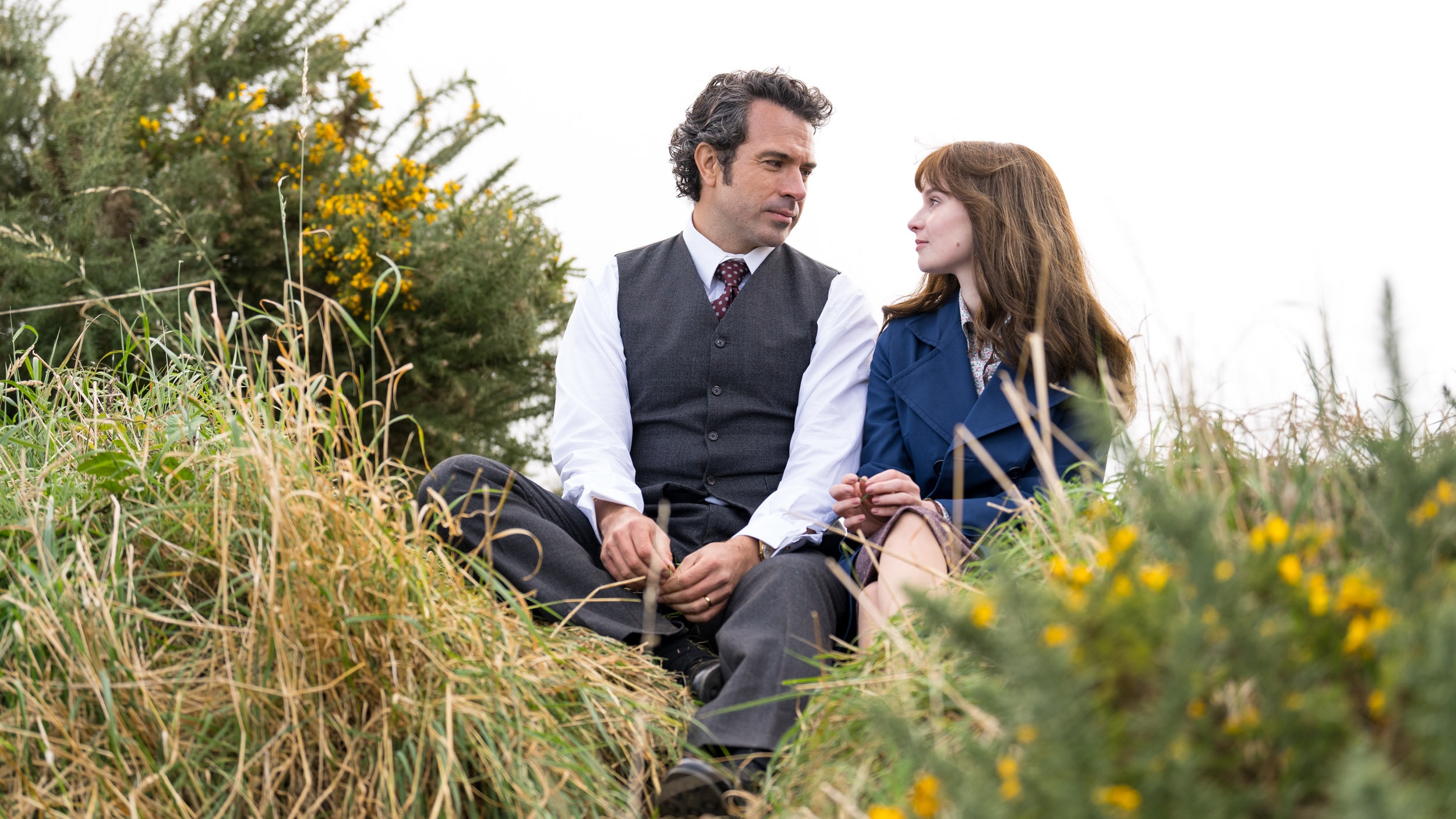 Cushla and Michael sitting in a grassy dune talking closely.