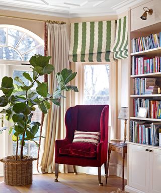 neutral living room with red velvet armchair, green and white striped blind and bookshelves