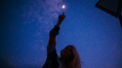 Young woman touching the moon on the dusk sky background