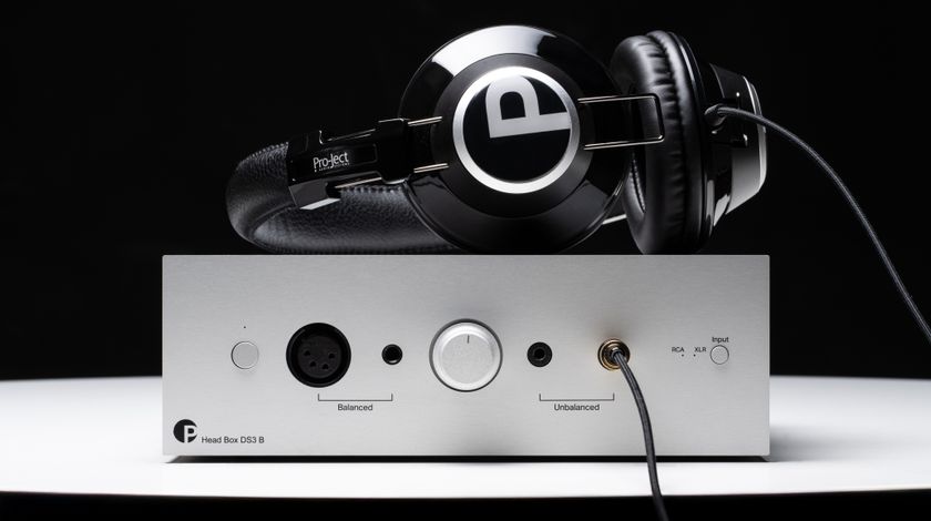 Pro-Ject Head Box DS3 headphone amplifier on a white surface with a pair of headphones plugged in
