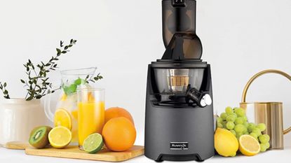 A Kuvings Juicer against a gray background, surrounded by fruits.