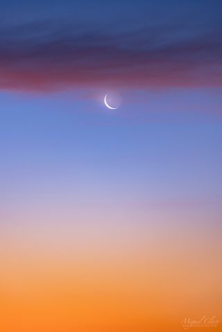 An orange glow signals the approaching civil twilight about 50 minutes before sunrise as the waning crescent moon shines behind a pink band of clouds.